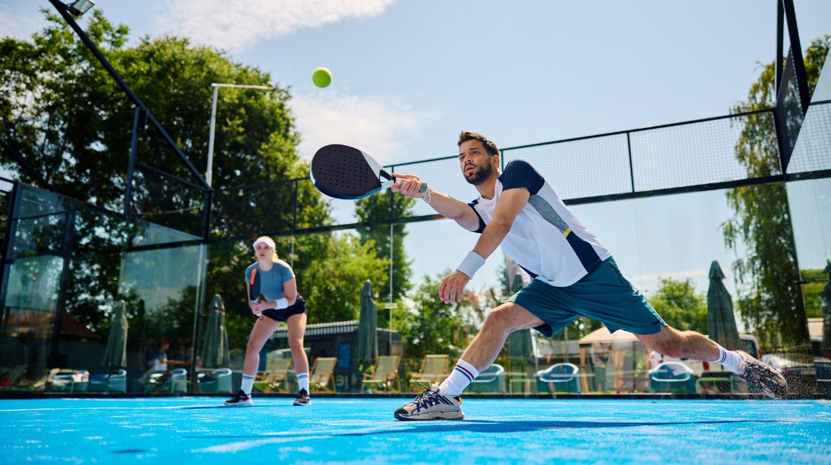 A man and his doubles partner play padel on an outdoor court.