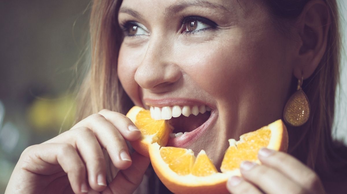 woman eating an orange, a good source of vitamin C