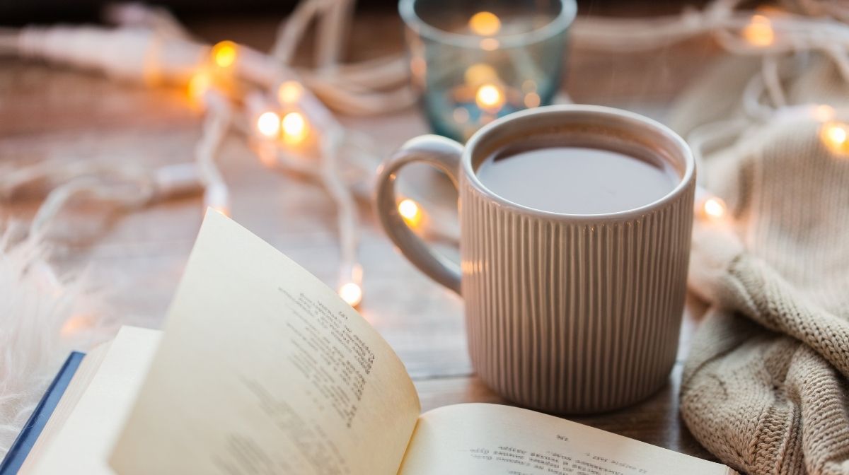 cosy set-up with candles, hot drink, fairy lights and book