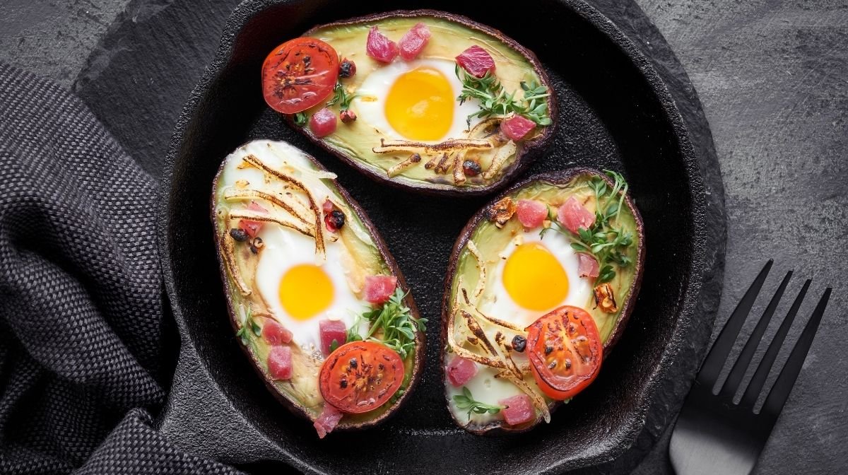 a keto-friendly meal of avocado baked eggs with ham and tomatoes