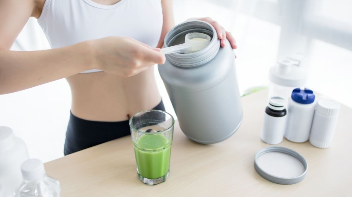 woman adding protein powder to a healthy green drink