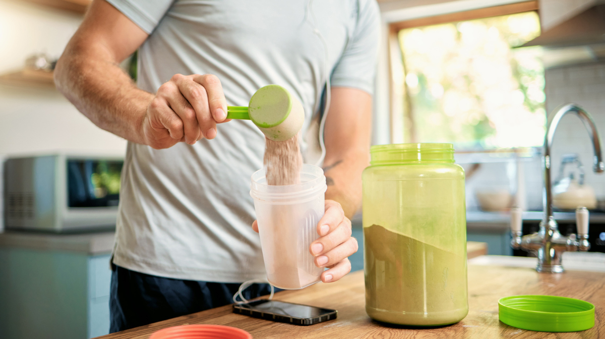 man pouring a scoop of protein powder into his shaker