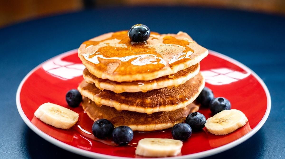 stack of pancakes on a red plate with syrup and blueberries on top