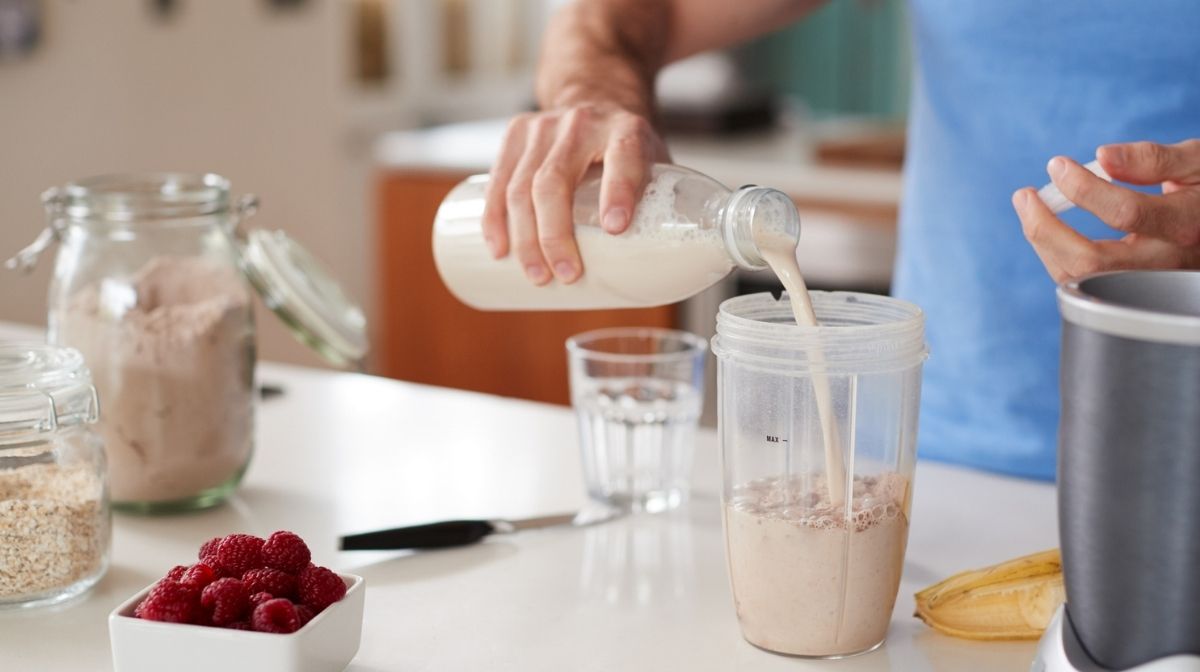 someone pouring milk into their blender to make a protein smoothie