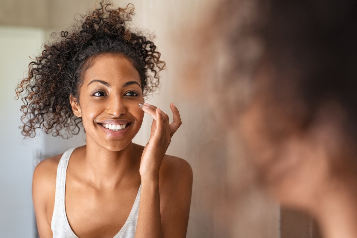 woman smiling into mirror while applying skincare routine to her face