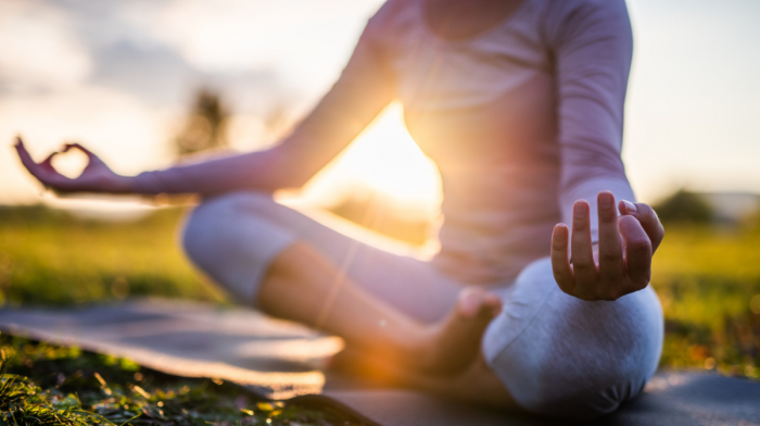 woman meditating outdoors with the sunset