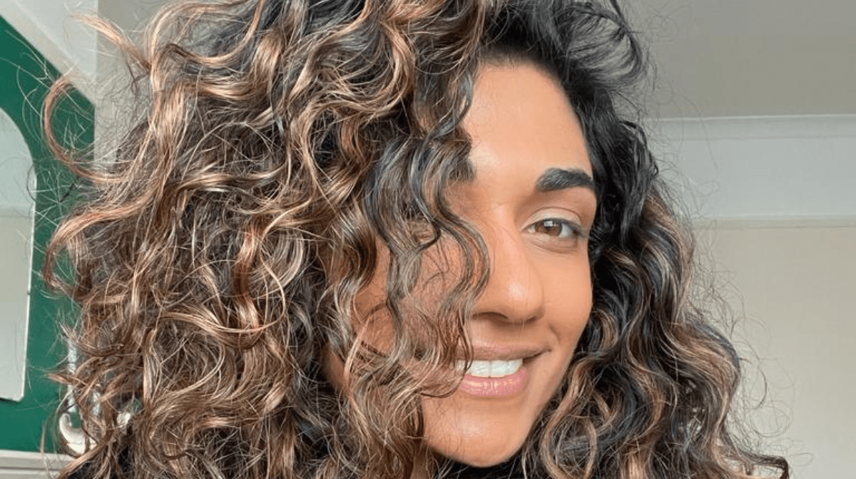 A woman smiling after doing her curly hair routine. 
