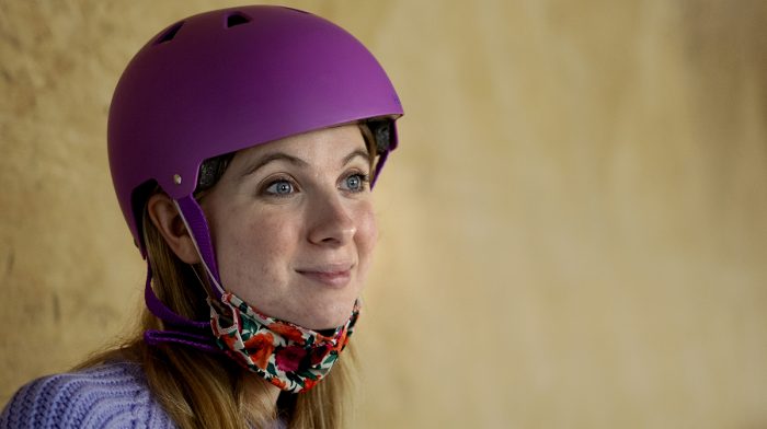 Image showing girl with a helmet on her head and a face covering pulled down to rest under her chin. She has acne