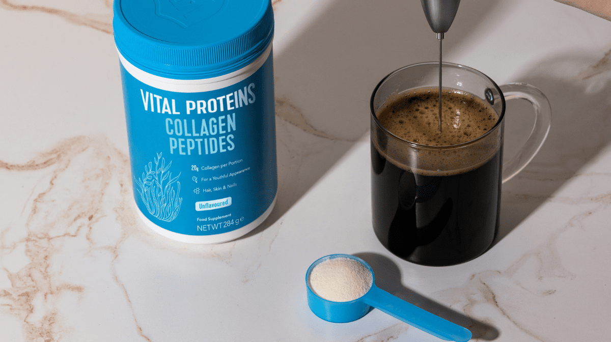 Vital Proteins Collagen Peptides Tin Standing next to a cup of coffee.