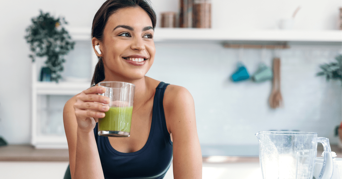 Athletic smiling woman drinking smothie while listening to music in her kitchen