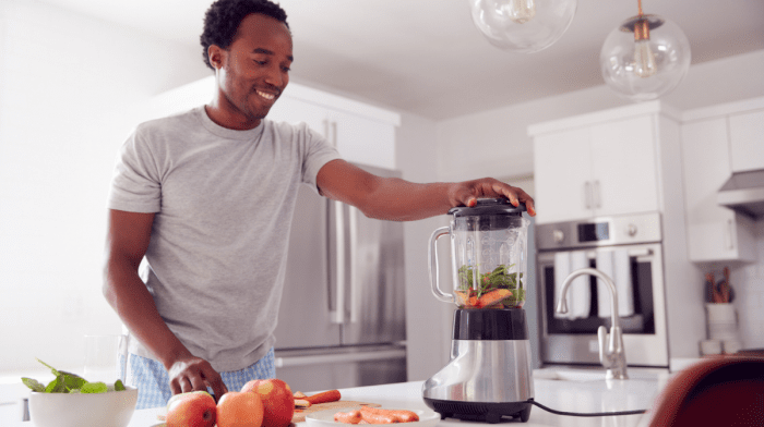 Man in Kitchen Putting Fresh Fruit And Vegetables in a blender making a collagen smoothie