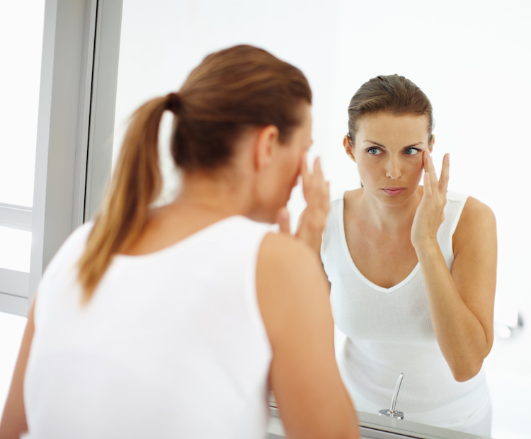 woman touching her eye in bathroom mirror