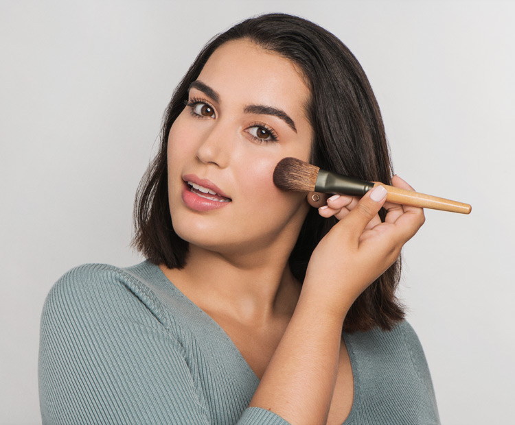 model applying blush with makeup brush