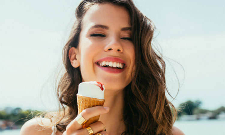 Woman with brown hair smiling while eating ice cream in the sun