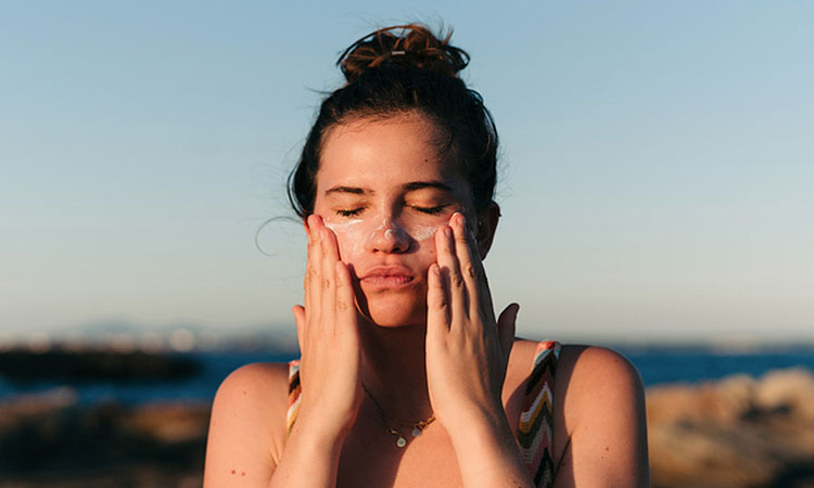 Woman at the beach applying white sunscreen cream to face