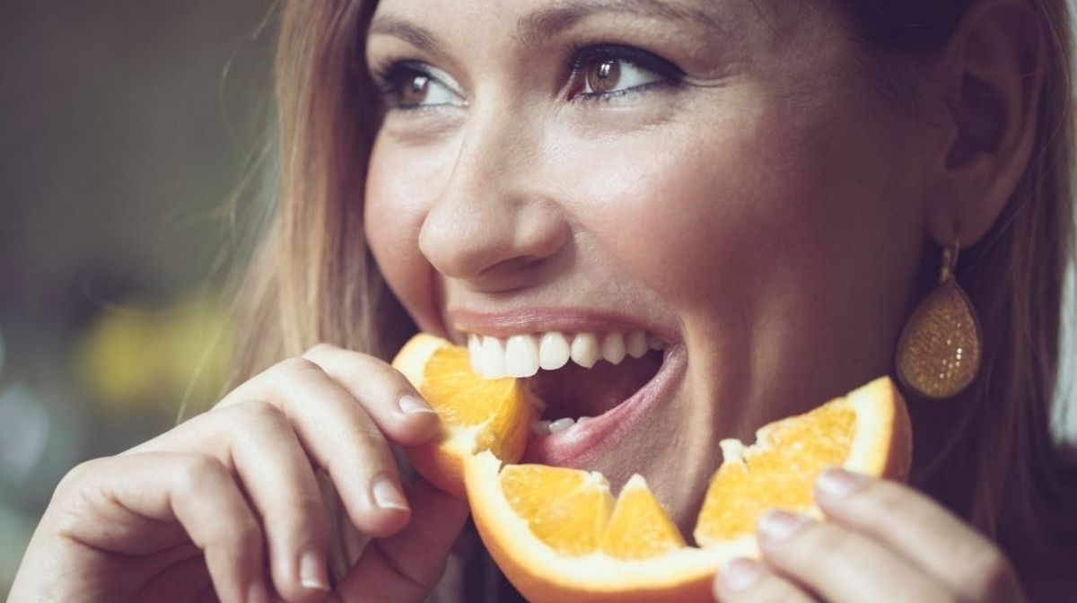 Как укрепить иммунитет и как оставаться здоровым. Девушка ест апельсин богатый витамином С и улыбается.