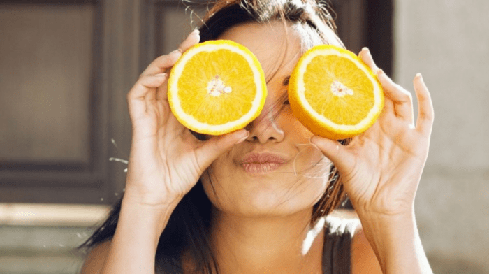 Девушка держит у глаз две большие дольки аппельсина и делает губы бантиком.