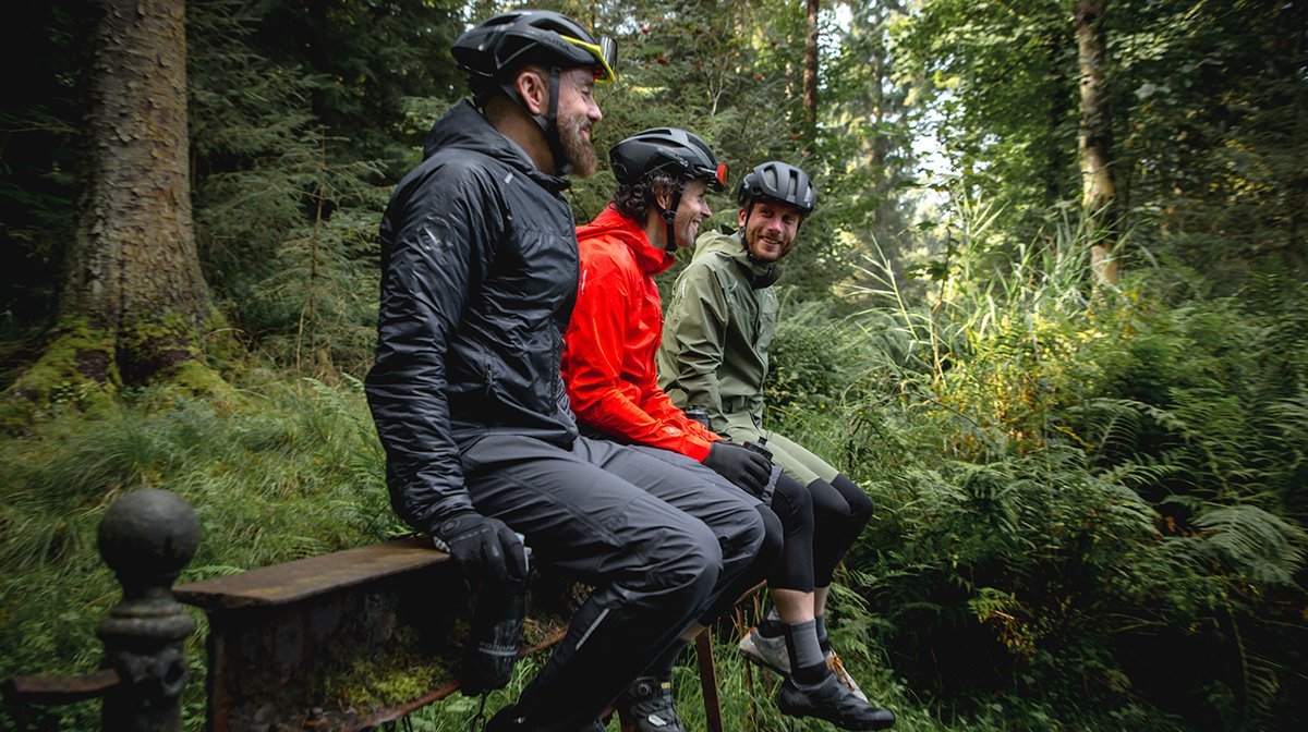 3 men sat on a bench in the woods wearing mtb gear