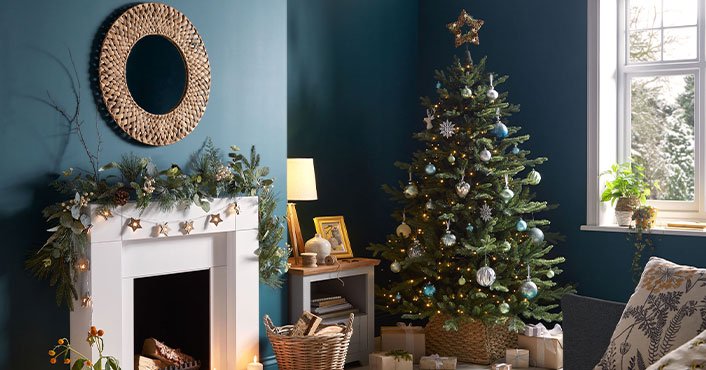 A decorated Christmas tree in the corner of a room against a teal-coloured wall