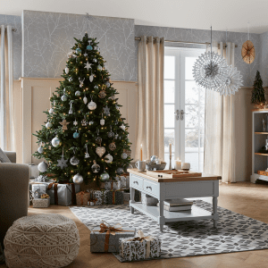 an image of a Christmas tree in a lounge with a rug, coffee table and sofa 