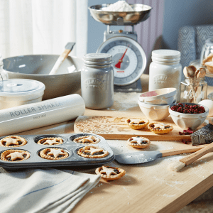 an image of mince pies in a baking tray with baking materials surrounding on a wooden table