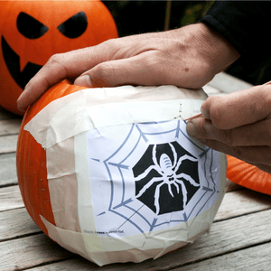 an image of a pumpkin design taped onto a pumpkin and being drawn over