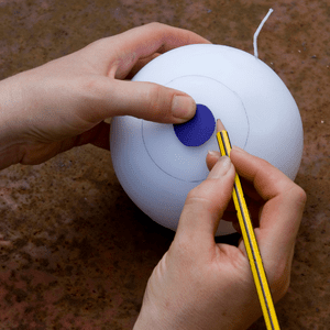 an image of an eyeball design being drawn onto a round candle 