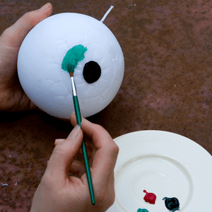 an image of a round candle being painted with an eyeball design