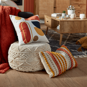 an image of cosy textured soft furnishings including a footstall and white and orange patterned cushions on a wooden floor