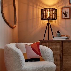 an image of a cosy white chair with a pink patterned cushion under the light of a table lamp 