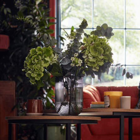 Glass vase holding leafy green plants.