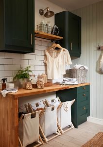 Photograph of a utility room with dark green cabinetry, under-counter fabric storage containers and a hanging rod