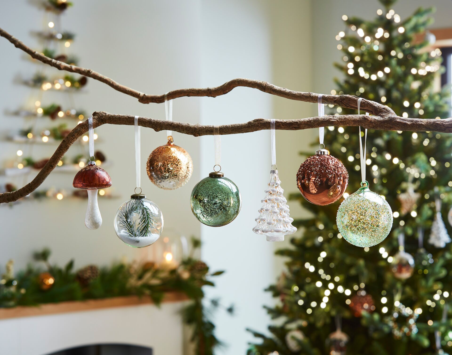 Photograph of tree branches decorated with Christmas baubles in front of a fireplace and Christmas tree