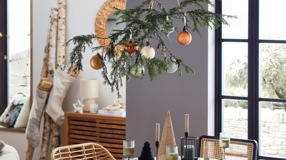 Festive pine branch hanging above table, decorated with orange, white and silver baubles.