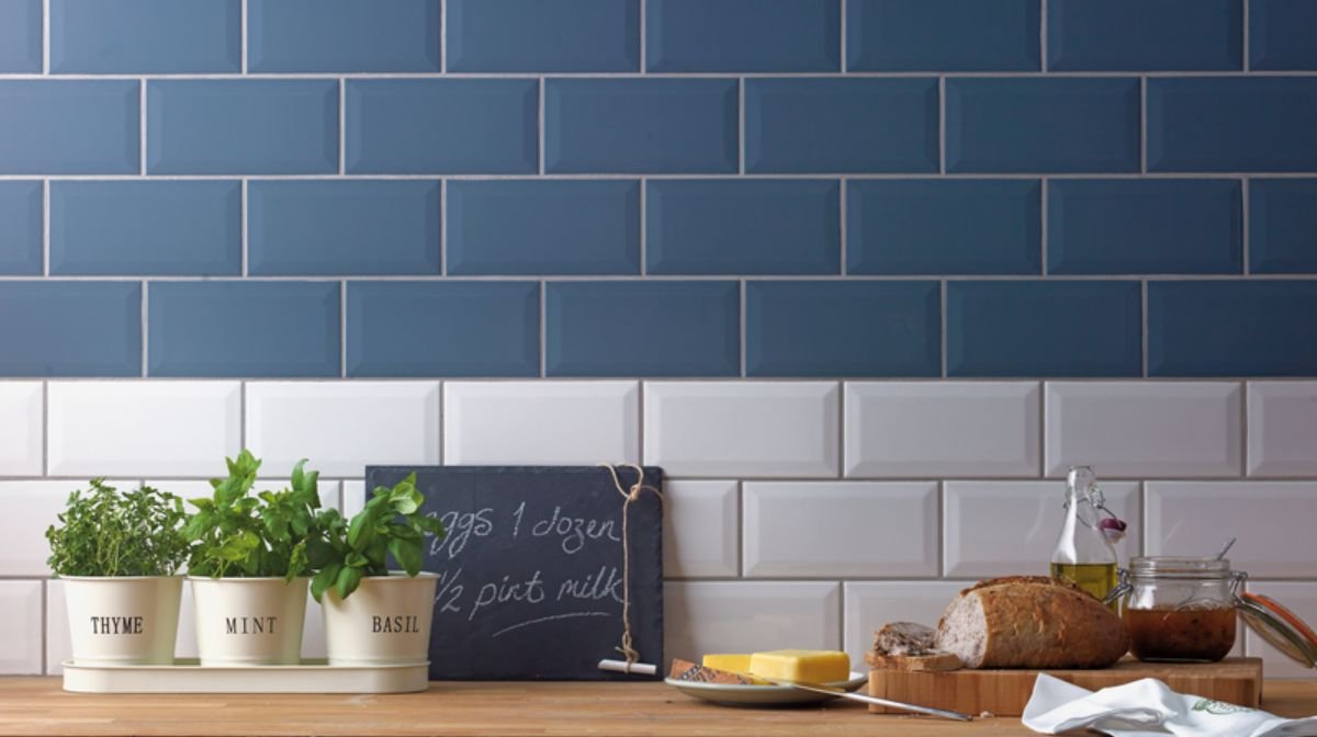 Image of a tiled blue and white kitchen splashback behind potted herbs on a kitchen worktop.