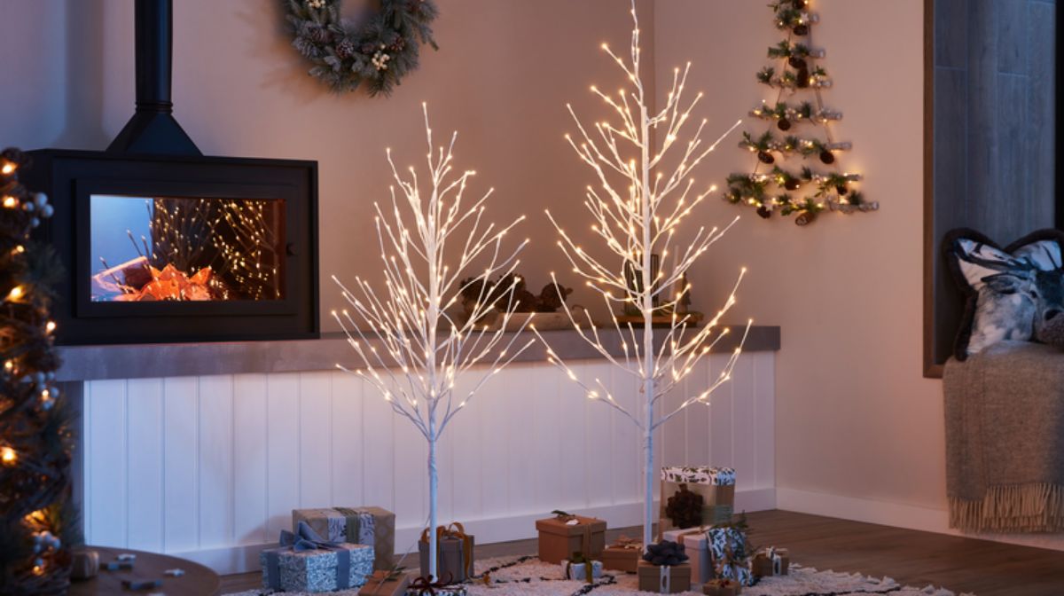 Faux white christmas trees with lights in festive decorated living room.
