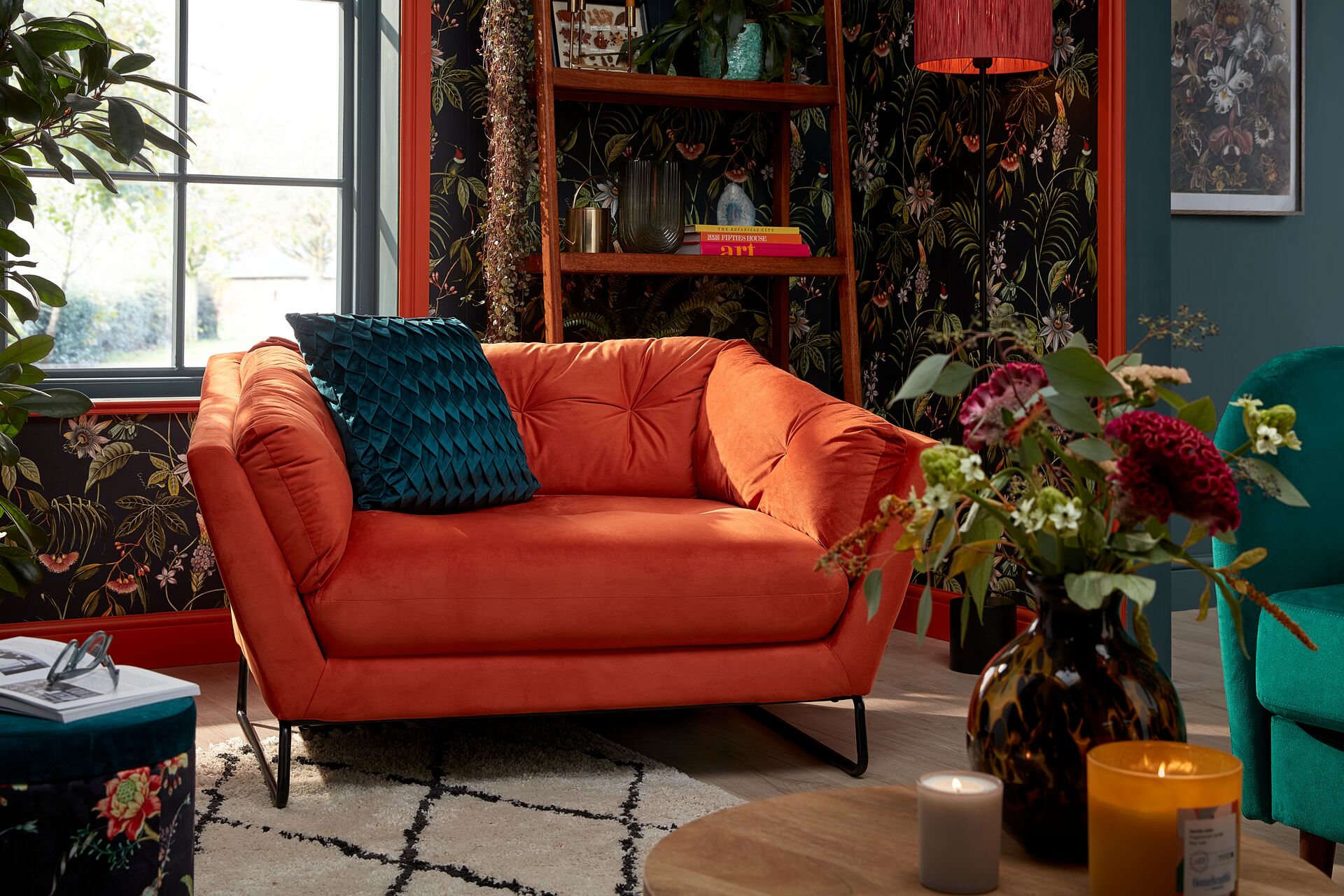 Living room furnished with bright orange sofa, floral wallpaper and ladder bookshelf