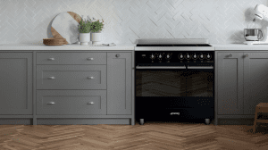 Photograph of a large freestanding oven in a modern grey kitchen with white tiled walls and a wooden herringbone floor
