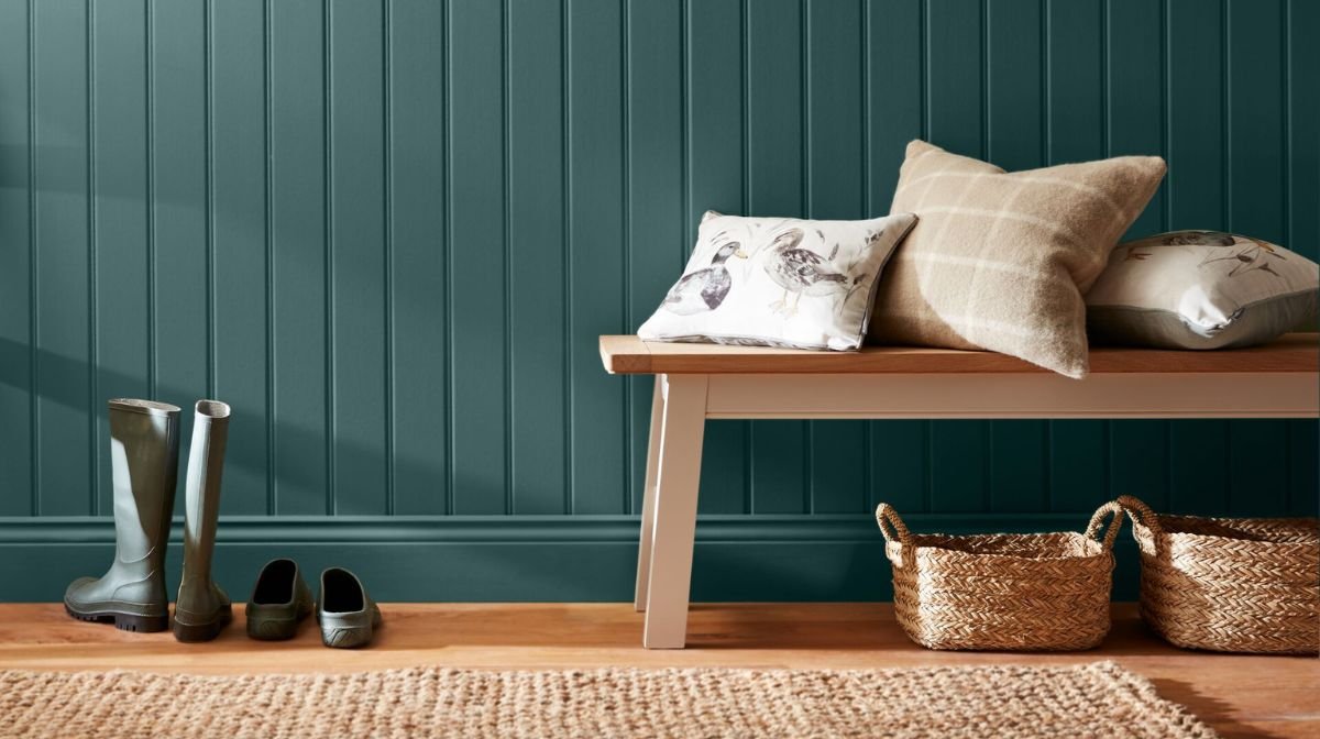 hallway painted deep teal, furnished with a bench, wellington boots and rattan carpet
