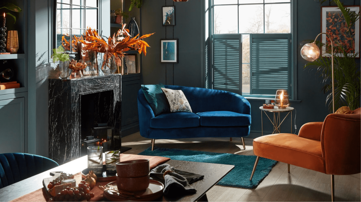 Image of a royal blue and orange velvet chaise longue positioned in a modern blue living room with a black marble fireplace and copper decorations