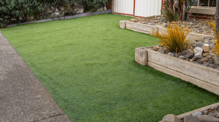 A view of artificial grass in a garden in between a path and bordered by planter boxes.