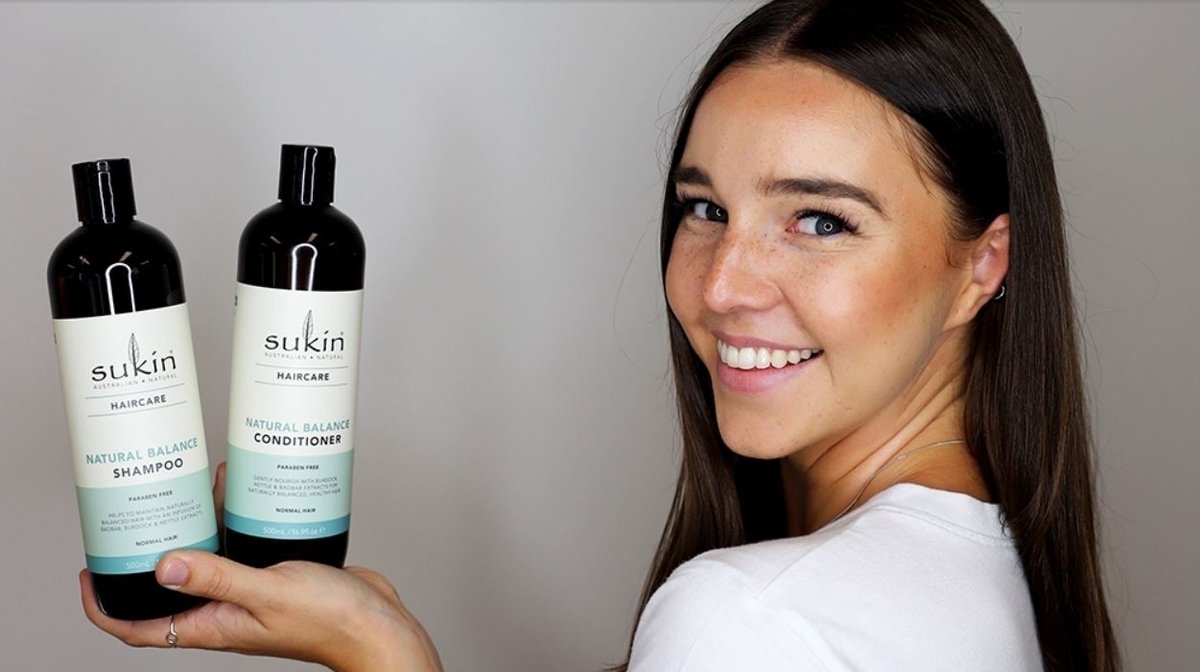 woman smiling and holding 2 bottles of natural haircare - a natural shampoo and natural conditioner