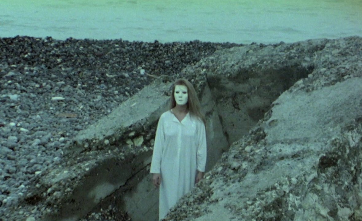 A woman wearing a white mask stands on a beach in Lost in New York (1989) 