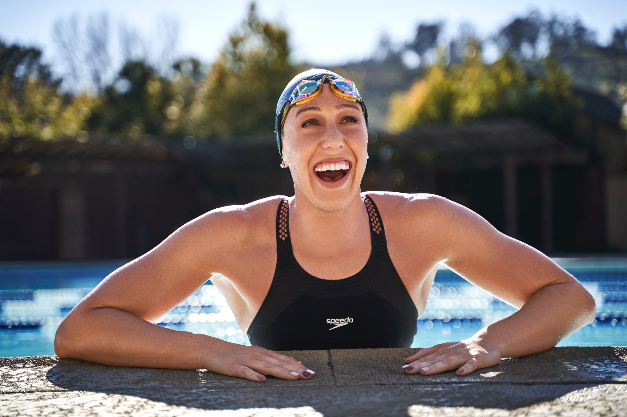 Abbie leaning on the side of a pool in Speedo gear