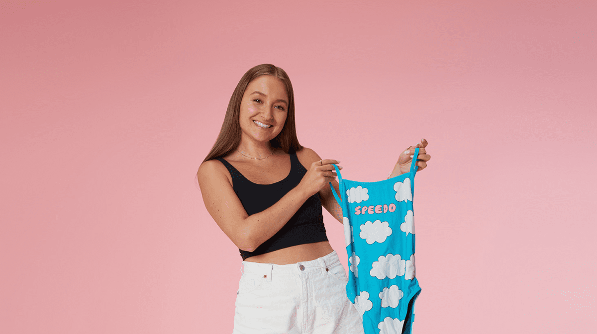 Tegan Price holding a blue swimsuit against a pink background