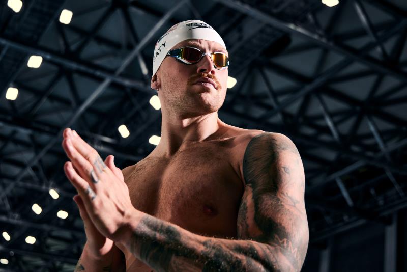Swimmer Adam Peaty preparing for a race wearing a swim cap and goggles.