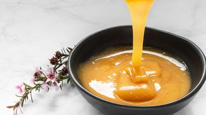 A black bowl filled with manuka honey standing on a white table decorated with flowers.