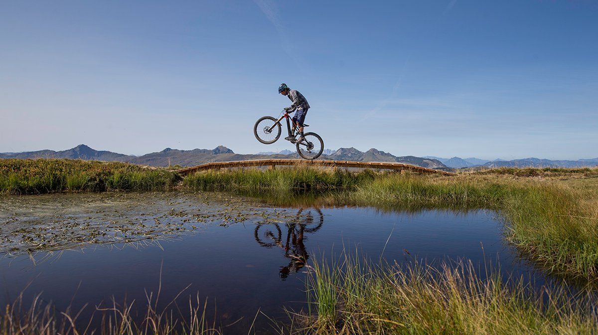 Rider bunny hops on mountain bike, reflected in pond