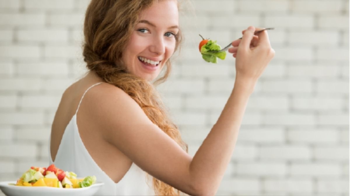 Una giovane donna che ride e mangia un'insalata con verdure e frutta che aiutano il sistema digestivo a rimanere in salute