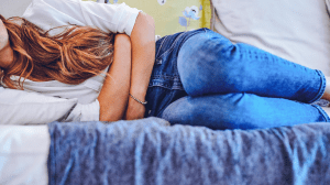 Una donna dolorante distesa sul letto con le sue mani piegate sulle pancia 